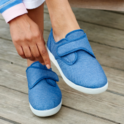 Someone putting on a blue pair of canvas strapped shoes